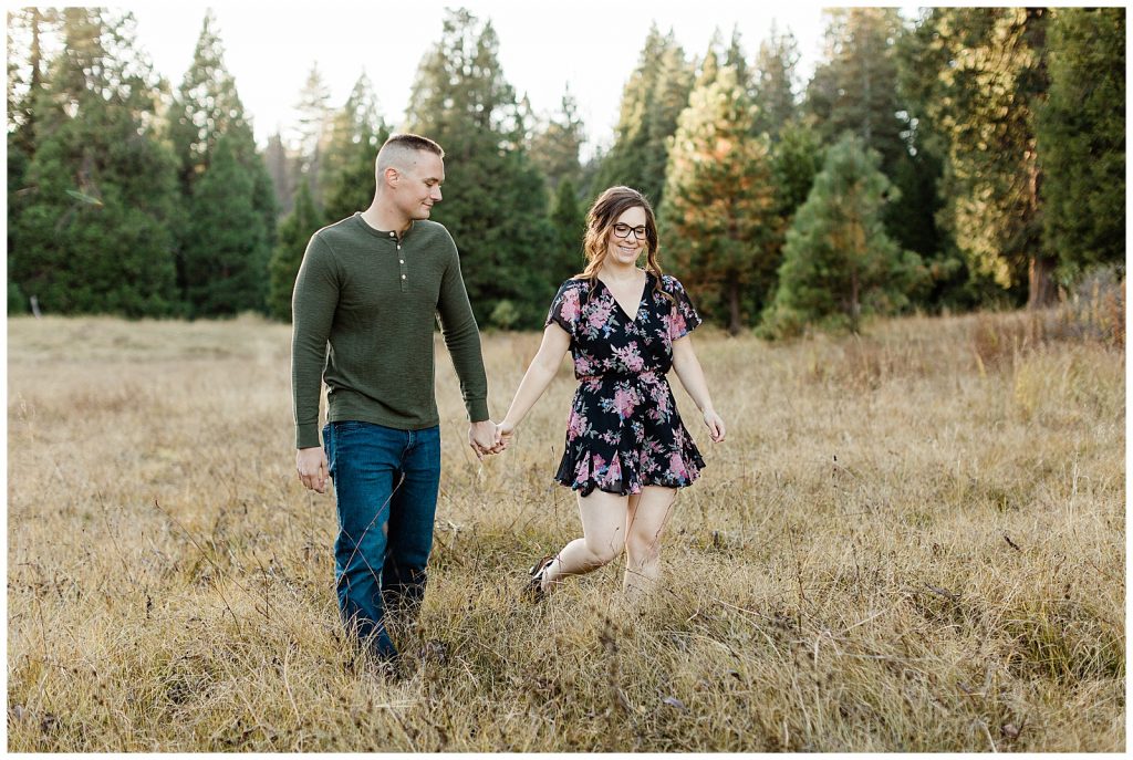 engaged couple walking through a mountain meadow holding hands