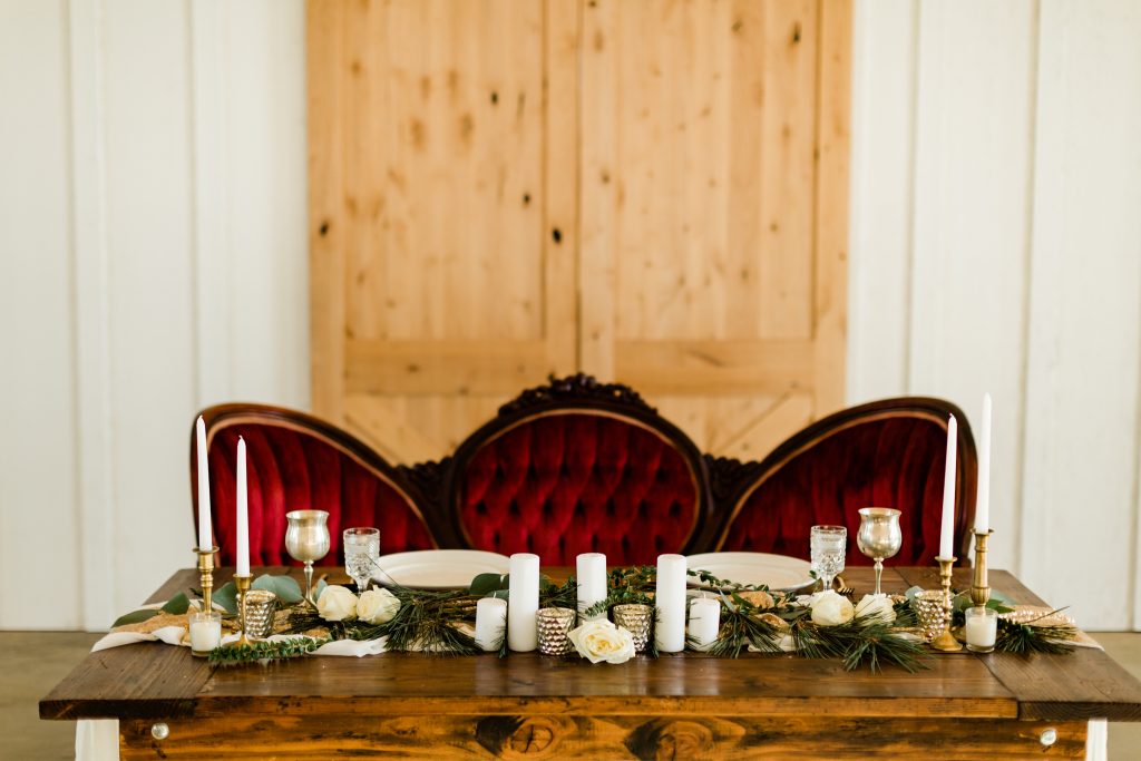 Rustic sweetheart table display with clear glassware, gold and white candles, a rich red vintage couch all rented from stockroom picks in fresno