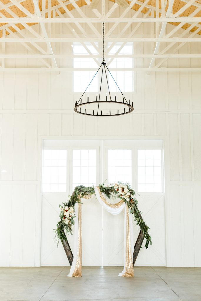 Geometric arbor decorated with christmas wedding florals for an indoor, white barn winter wedding ceremony at R&C Ranch in Fresno, California.