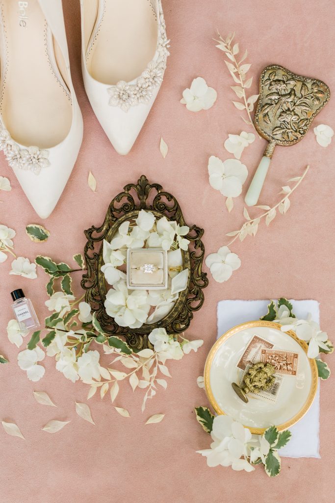 blush and white flat lay with ring, shoes, stamps, flowers