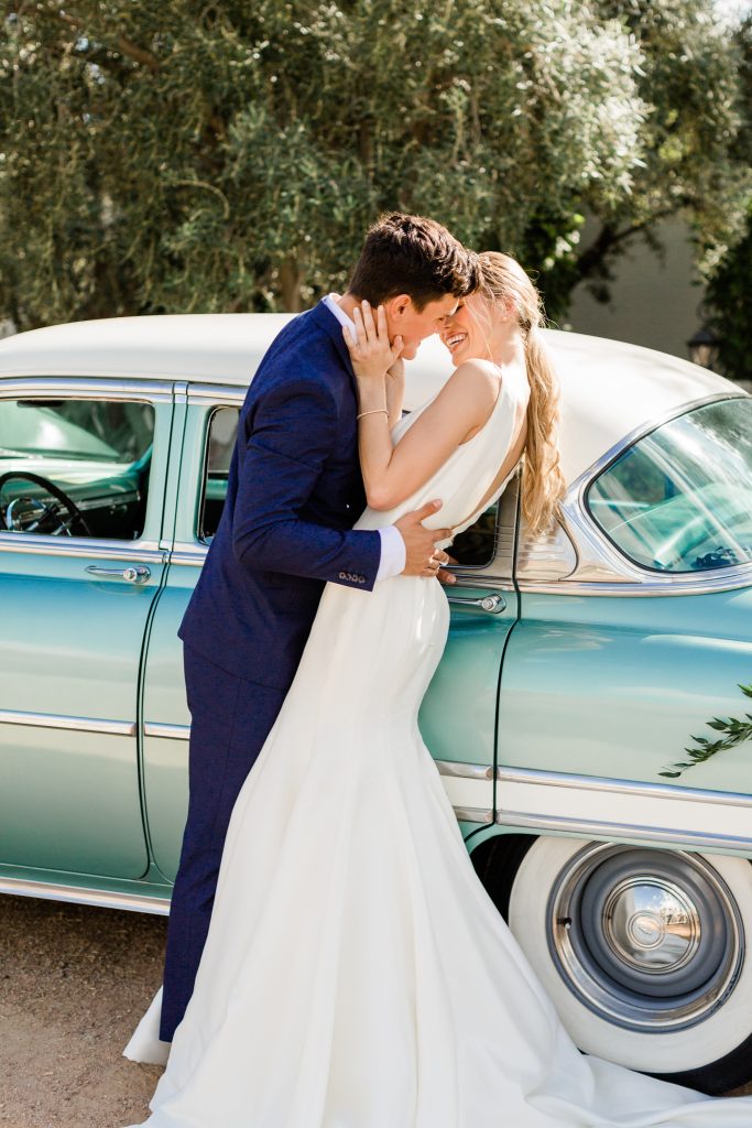 groom in navy leaning in to bride in front of vintage car