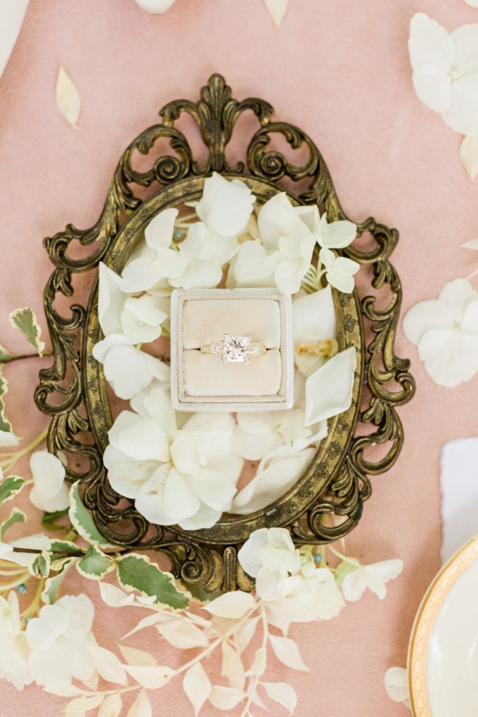 close up of wedding ring in Mrs Box with white petals and blush backdrop