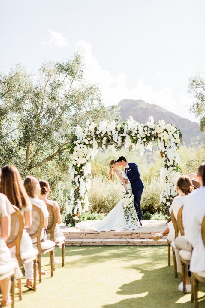 bride and groom at ceremony with white floral arch