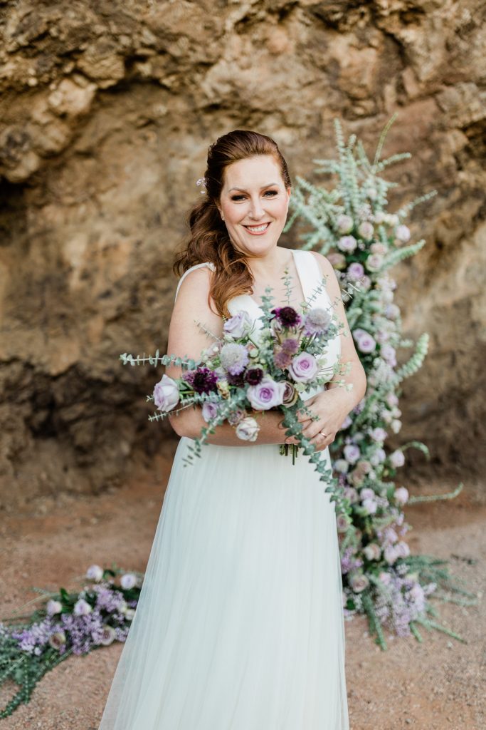 bride smiling and holding a wedding bouquet with lavender and dark purple flowers