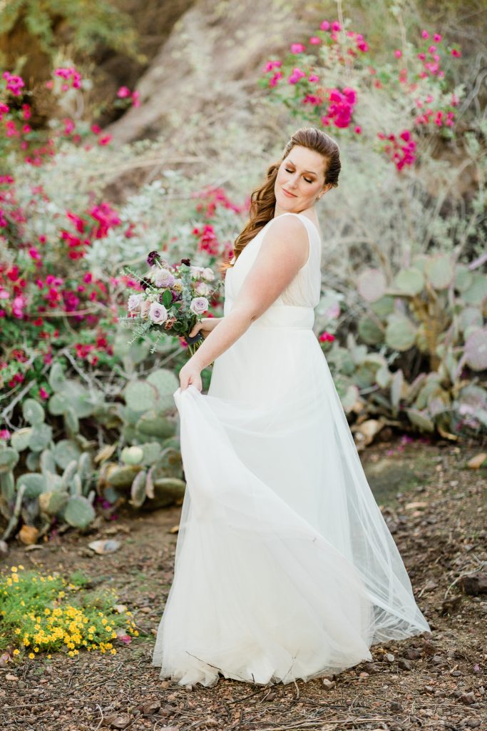 red headed bride twirling in a Jenny Yoo chiffon wedding dress with cactus and purple flowers in the background for a desert bridal session