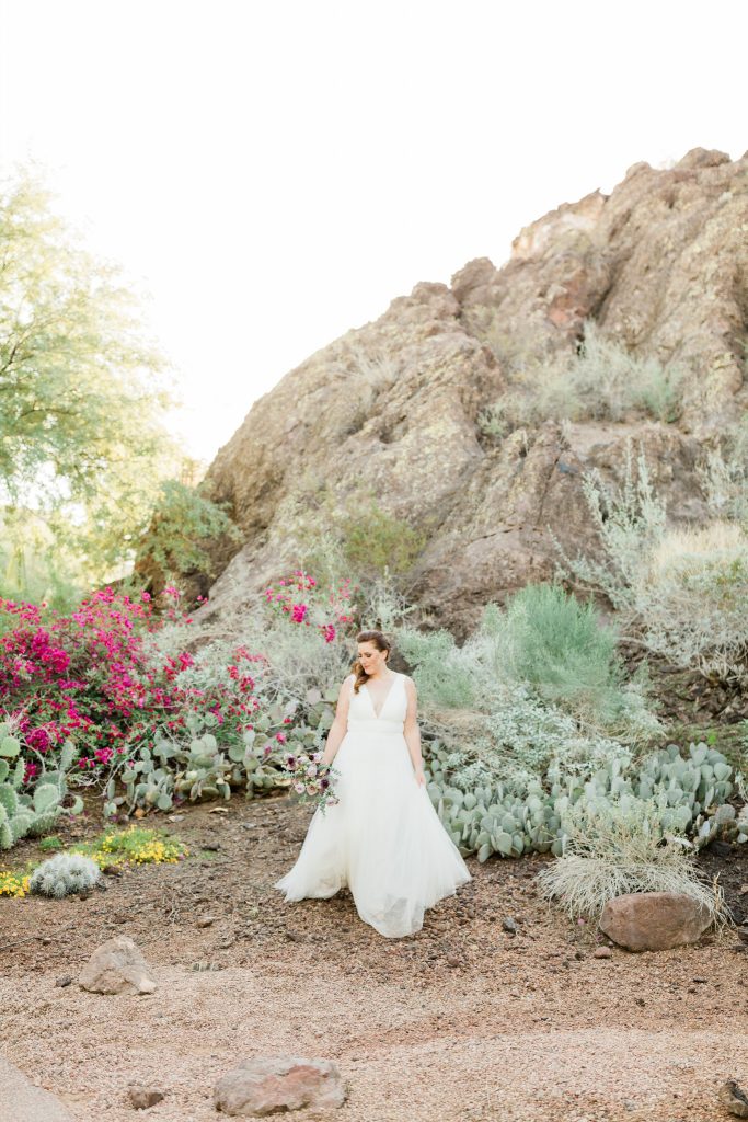 desert bridal session portrait of a bride walking and holding a bouquet in front of a cactus garden with pink flowers