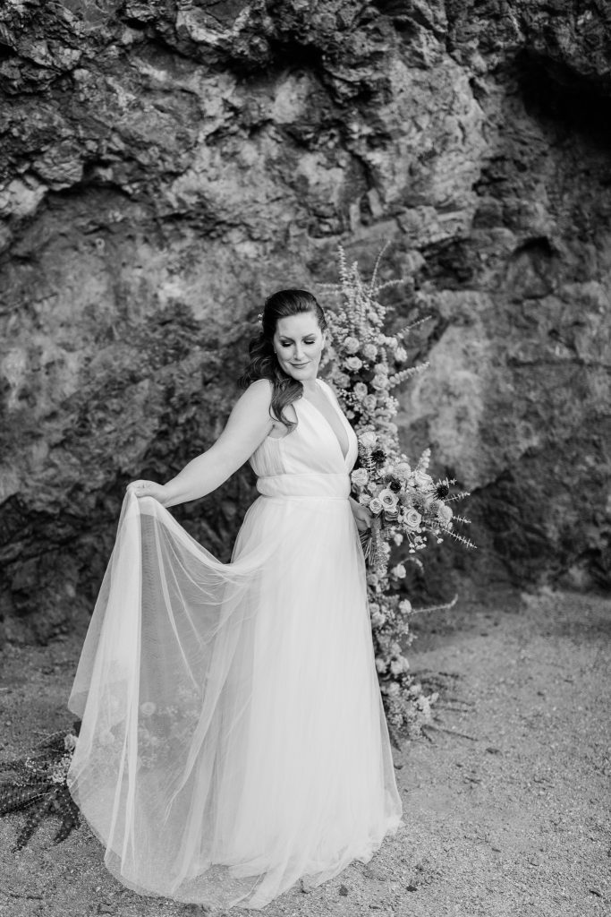 black and white image of a bride holding her chiffon wedding skirt in the desert
