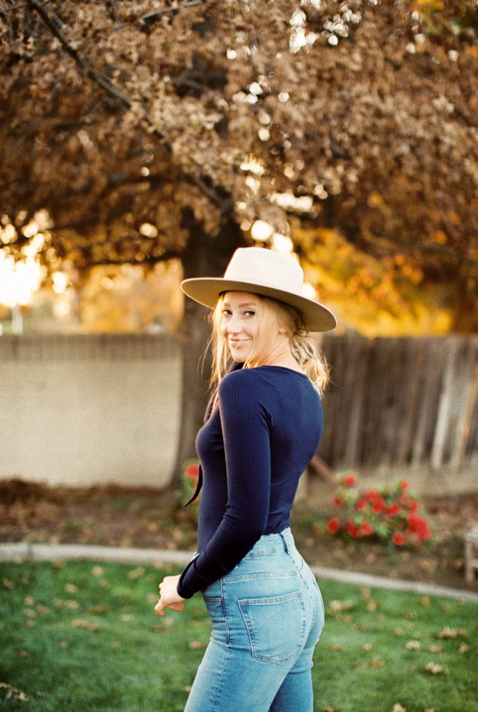 blonde woman wearing a beige suede hat, a navy blue shirt and high waisted jeans