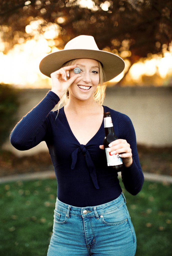 woman holding a beer bottle cap over her eye and smiling