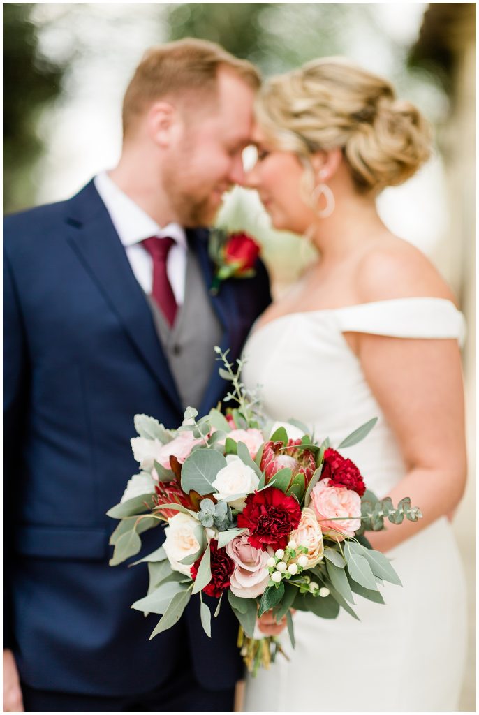 focus on pink and red bridal bouquet with couple in blurred background