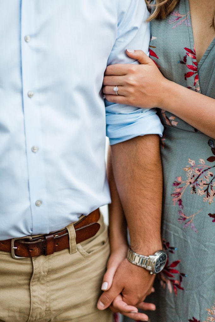 close up of an engaged couple holding hands with her engagement ring showing