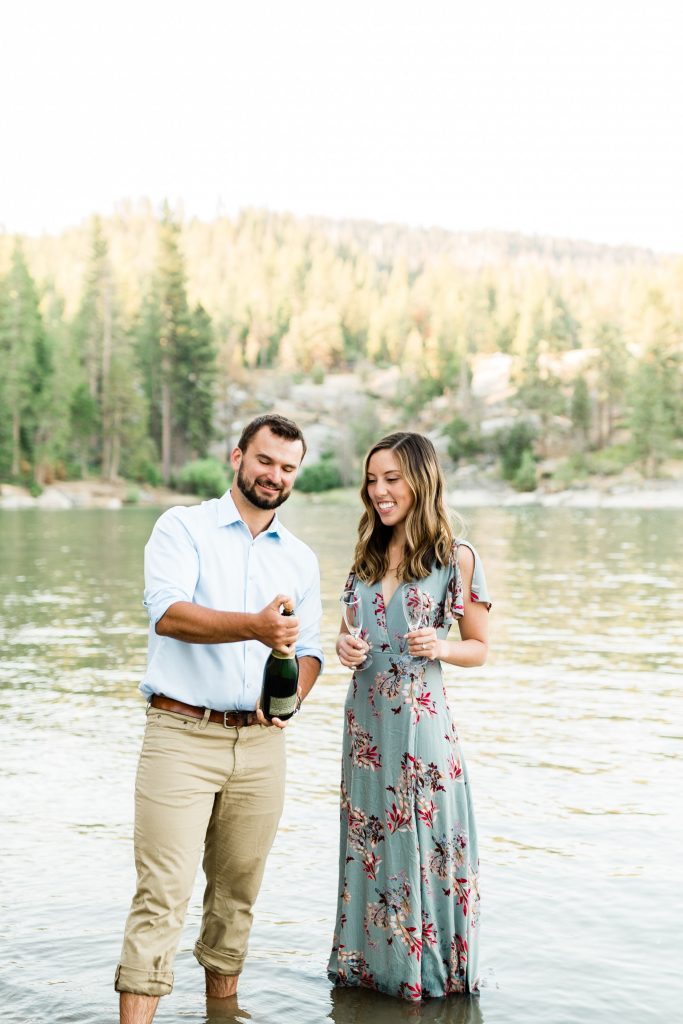 couple popping champagne on the shores of a california lake