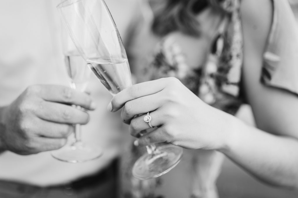black and white close up of a couple holding champagne glasses and cheers-ing