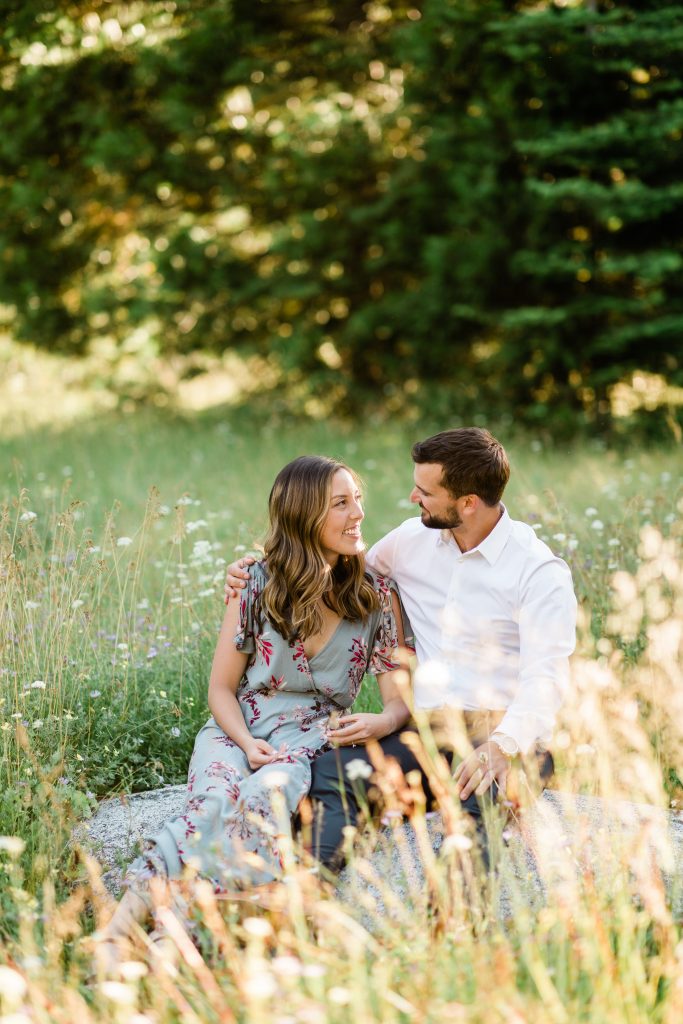 couple sitting on a rock smiling in a wildflower meadow at sunset