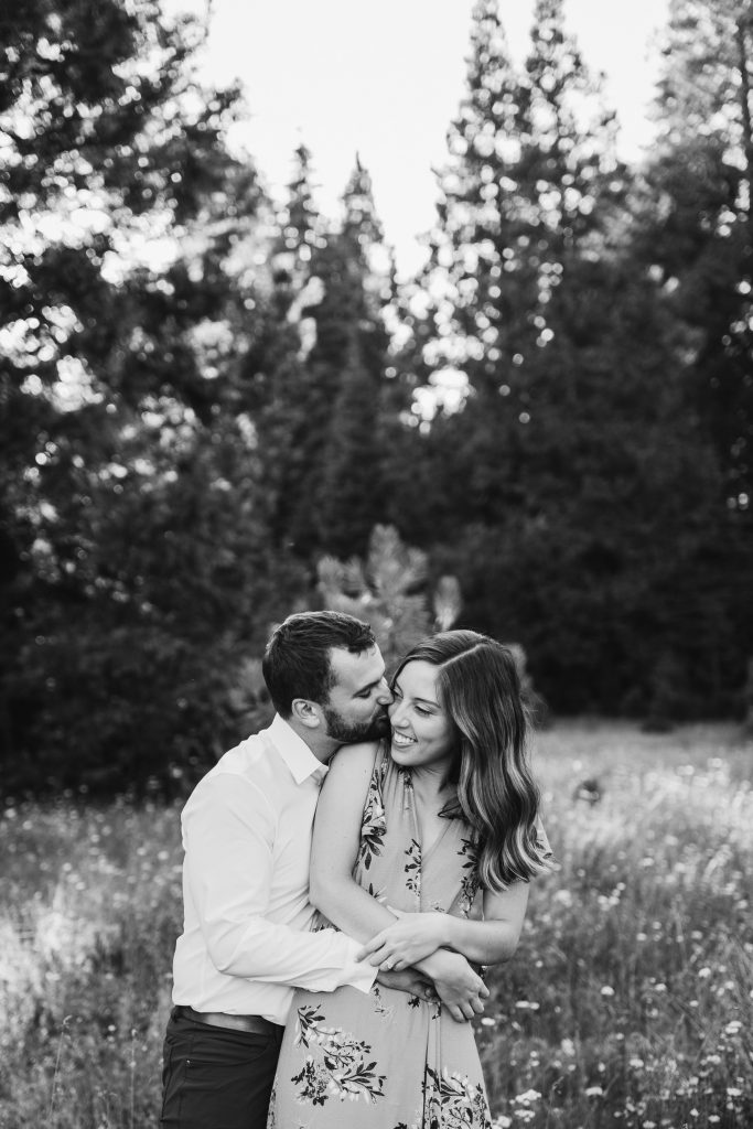 black and white shot of a couple embracing while her fiance hugs her tight and kisses her cheek