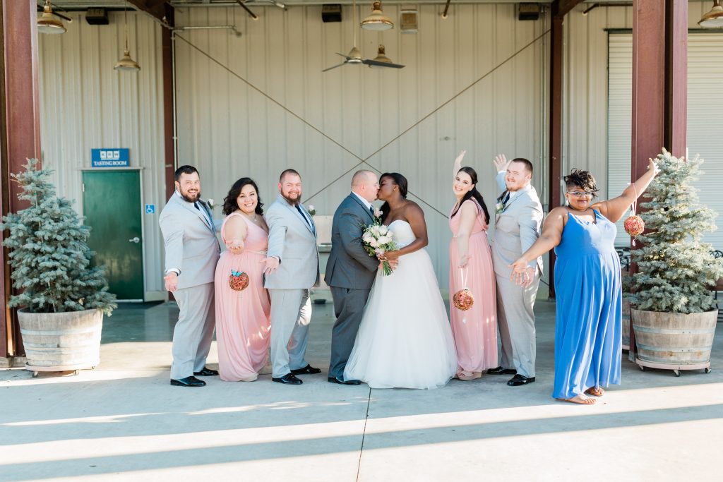 fun wedding party photo while bride and groom kiss