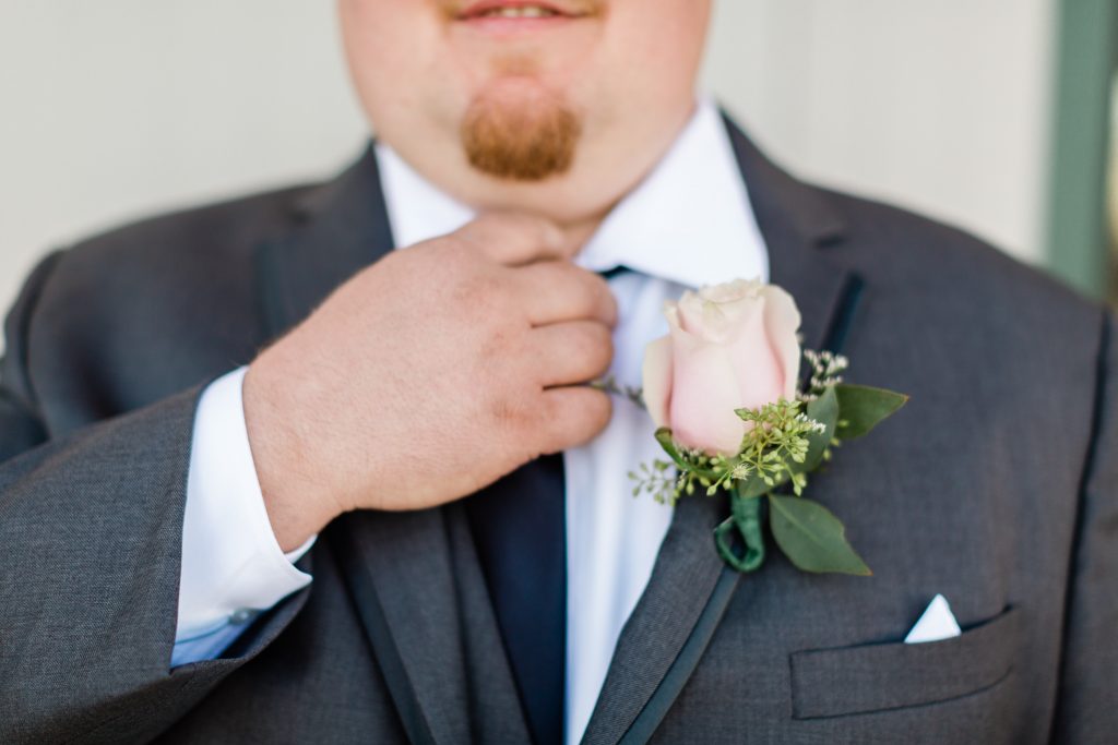 close up of groom fixing navy tie with pink rose boutonniere