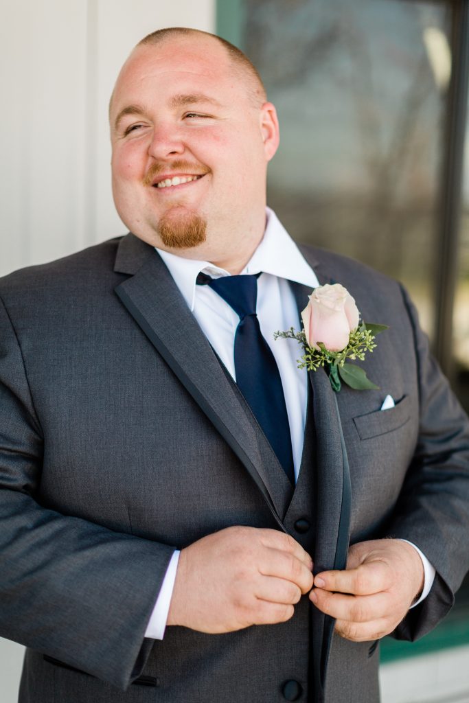 groom buttoning grey suit and smiling looking away