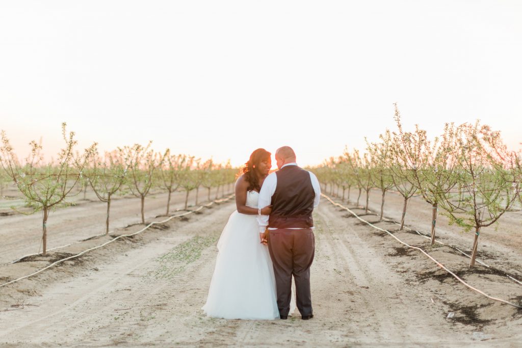 bride and groom in tree lined field at sunset