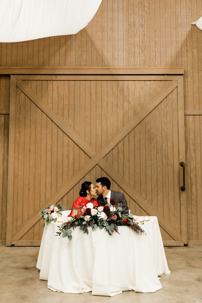 married couple kissing while sitting at their sweetheart table in front of barn doors at kings river winery