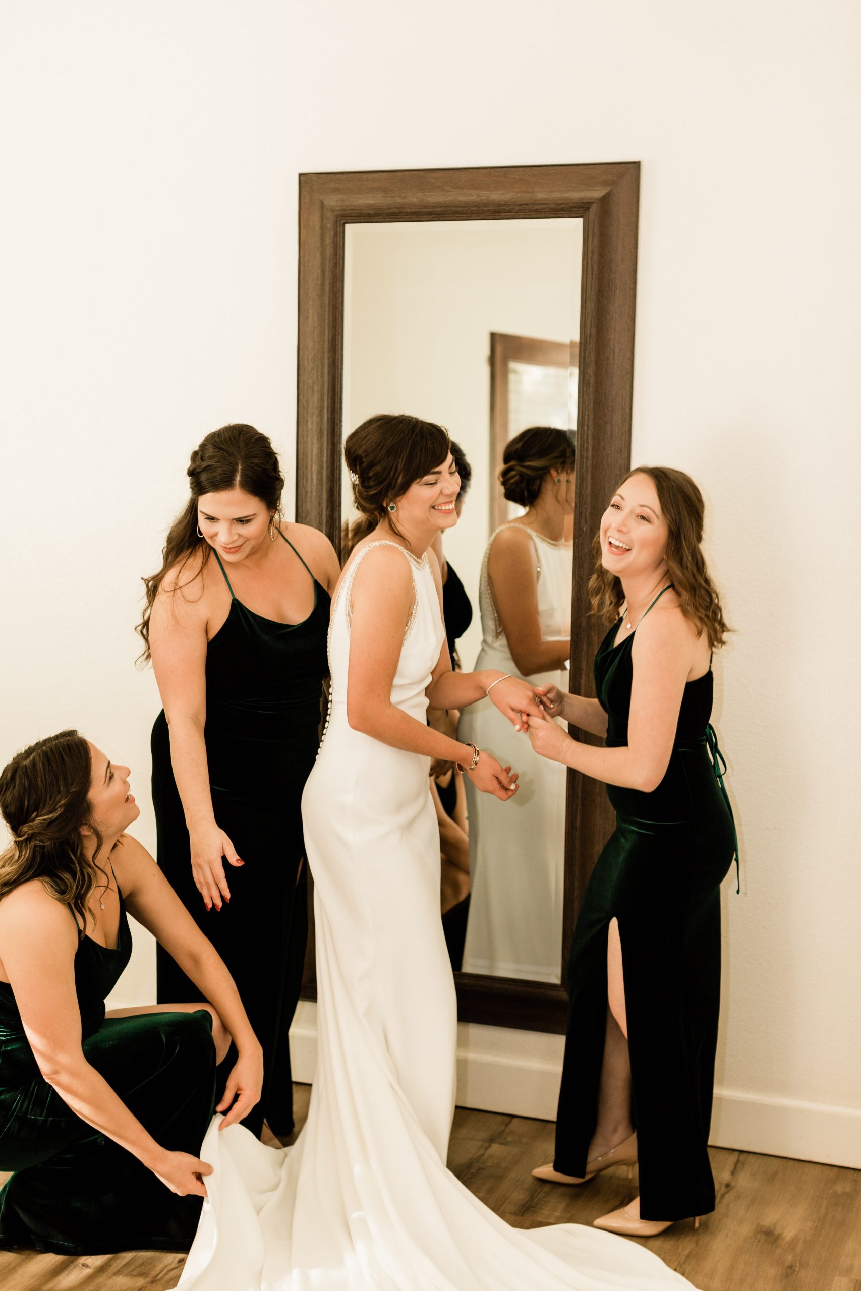 bridesmaids helping bride into wedding dress and laughing