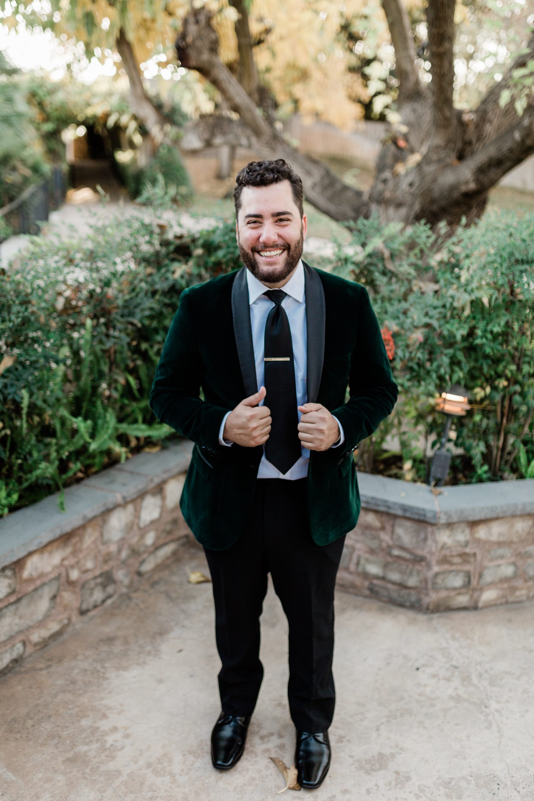 groom smiling in green velvet suit jacket before sunset wedding ceremony