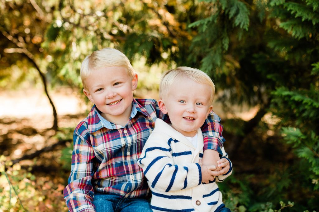 two blonde brothers sitting on a log and smiling