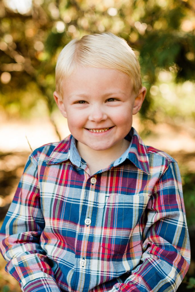 young boy smiling in a maroon and blue plaid shirt