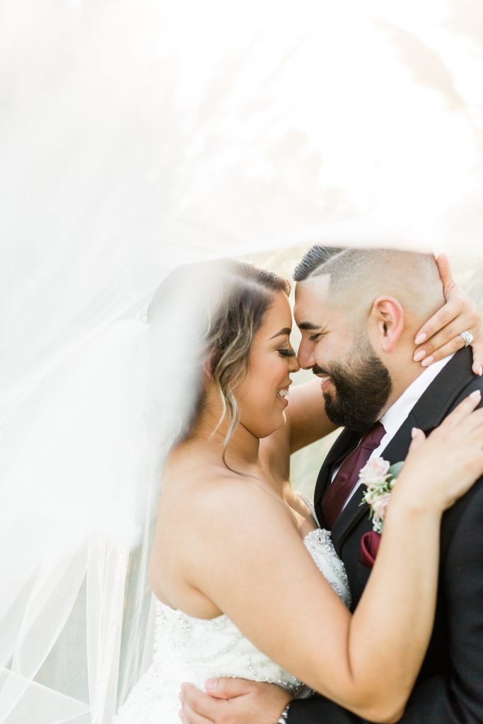 bride and groom touching noses and smiling with their eyes closed with the bridal veil sweeping in front of the camera