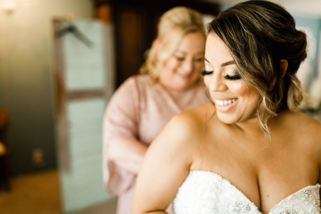 bride smiling while her mom zips up her wedding dress