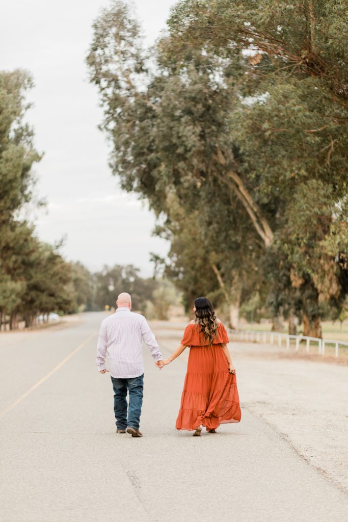 engaged couple holding hands and walking along an open road