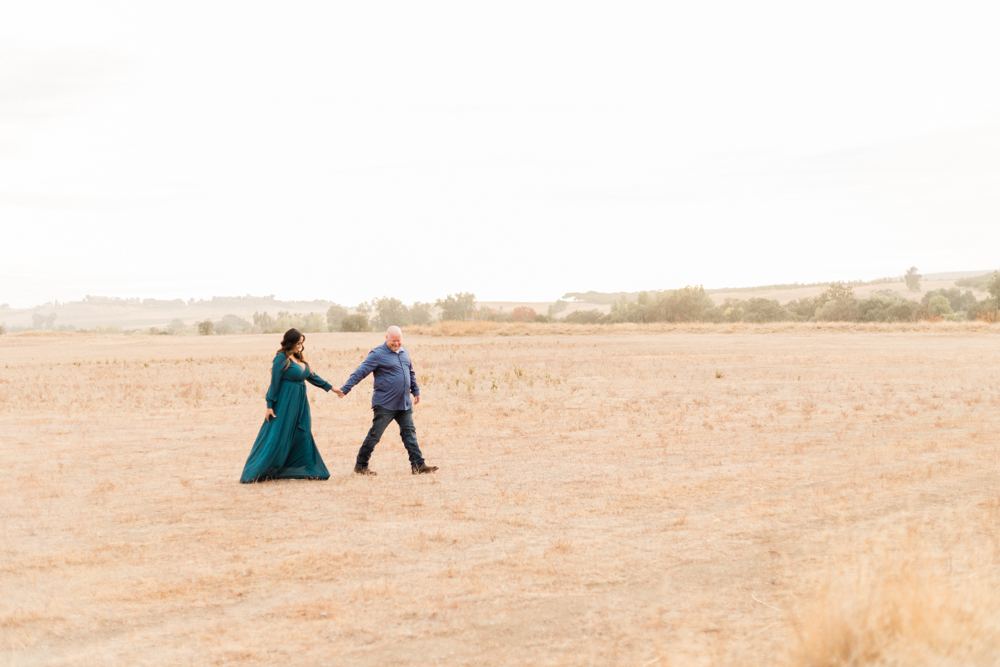 engaged couple walking through an open field