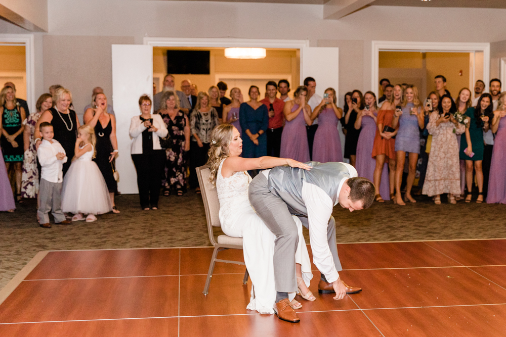 Groom dancing on bride while she sits in a chair and people look on
