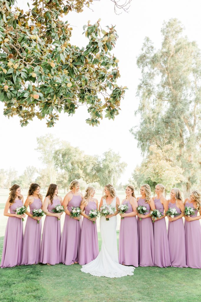 Bridesmaids in a line looking at bride in light purple dresses with bouquets