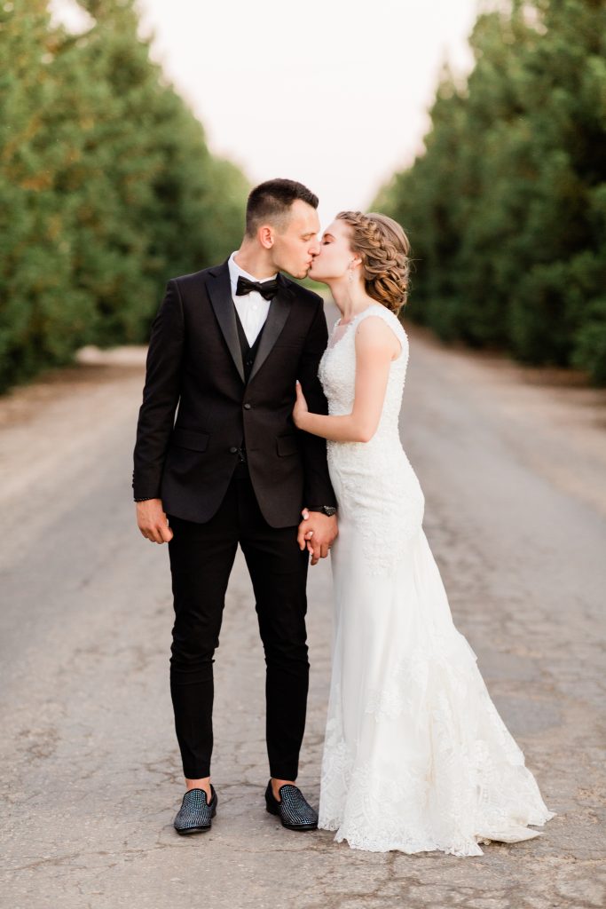 bride and groom kissing along a road lined with trees