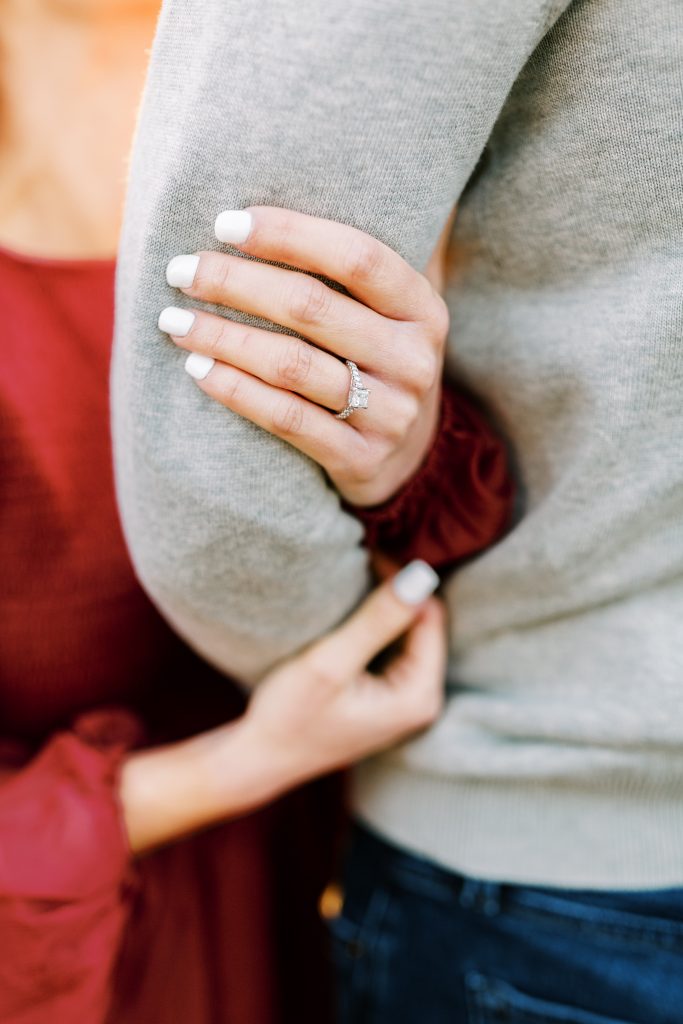 close up of engagement ring while holding fiance's arm with white nails