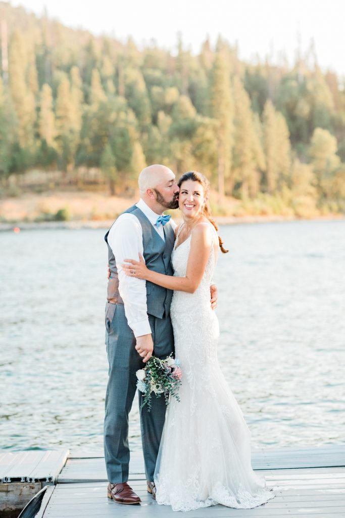 Bride smiling while groom kisses her cheek on bass lake dock