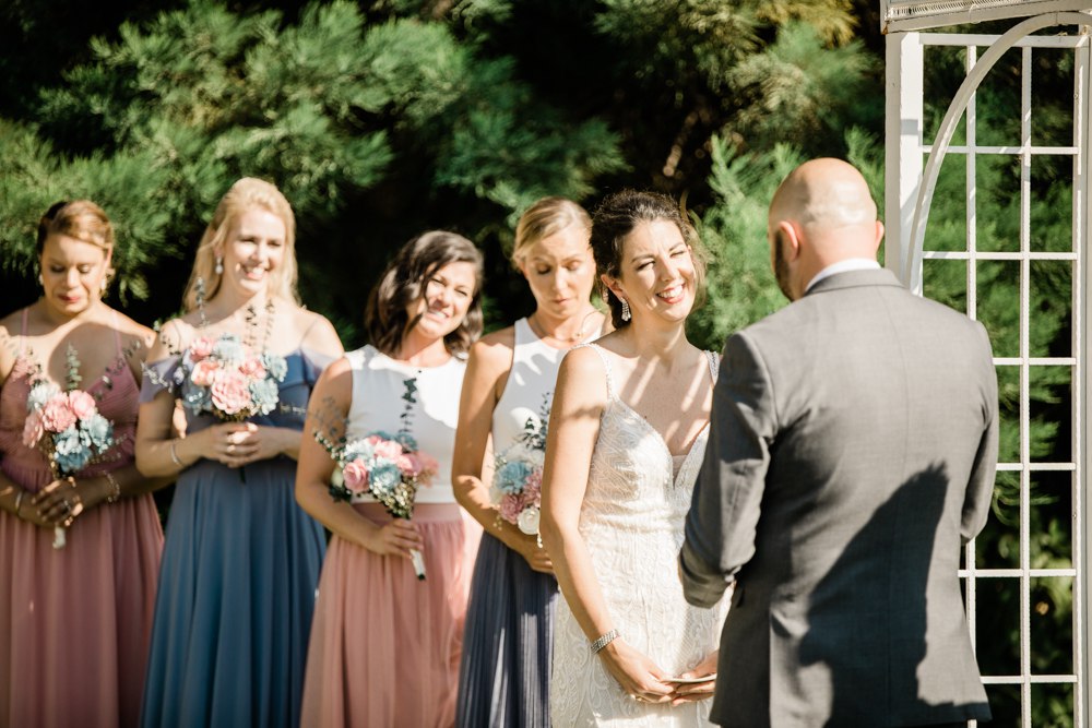Bride smiling while bridesmaids smile and cry during ceremony