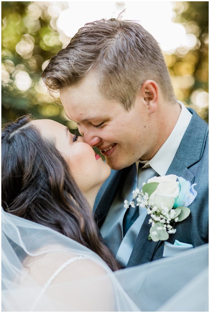 Couple leaning in to kiss while veil blows in the wind. 