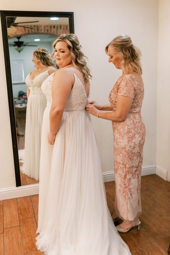 Bride's mom button her wedding gown in front of a mirror