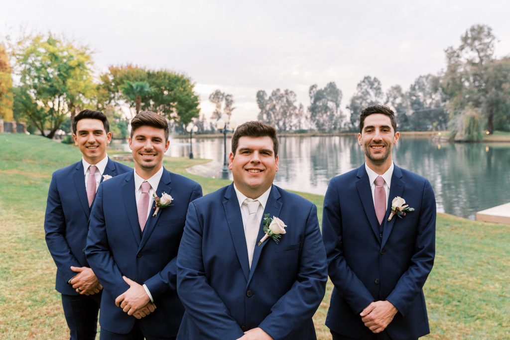 Groomsmen in navy with blush ties in front of Wolf Lakes Park on an overcast wedding day
