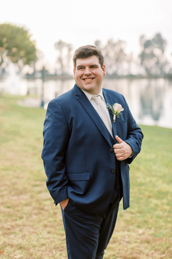 Groom smiling in navy with a white tie and white rose