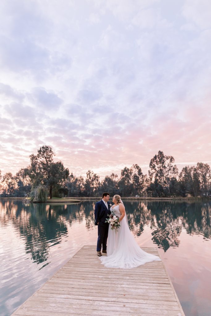bride and groom standing on dock at pink sunset at wolf lakes park a fresno wedding venue
