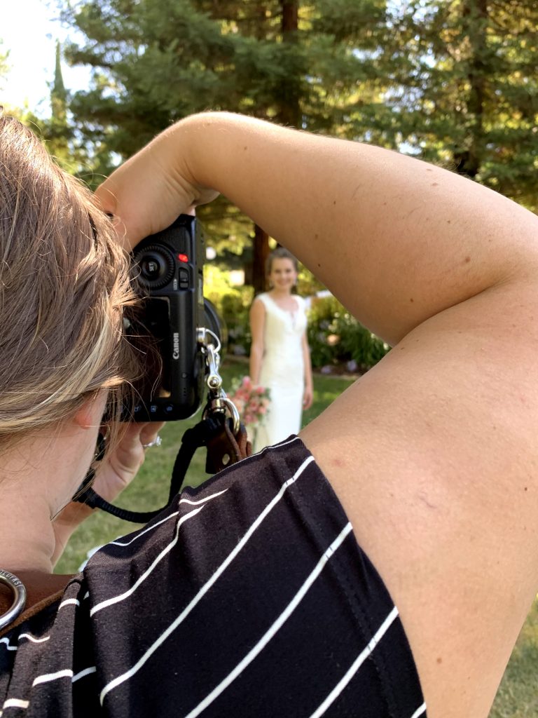 View of bride through photographers arm and camera
