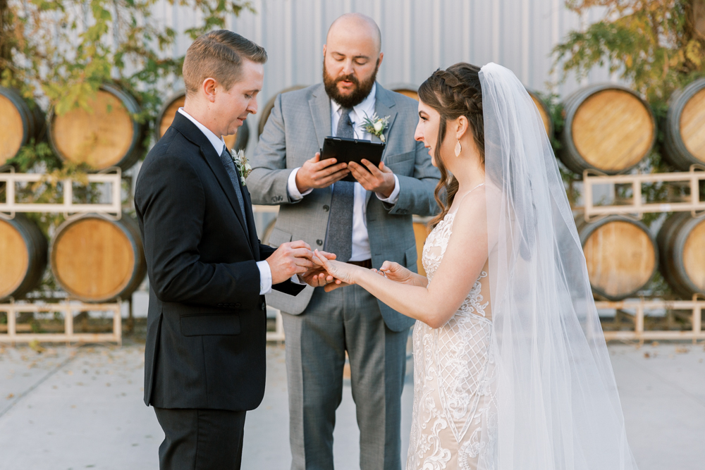 Groom putting ring on Bride while officiant recites vows. 