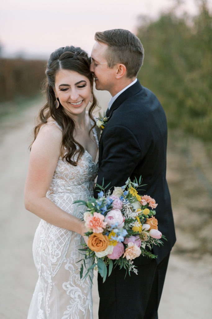Groom whispering to bride while she holds colorful bouquet.