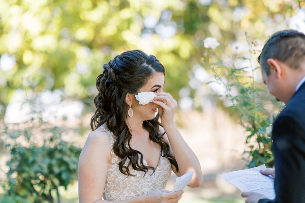 Bride wiping her eyes after reading grooms written vows. 