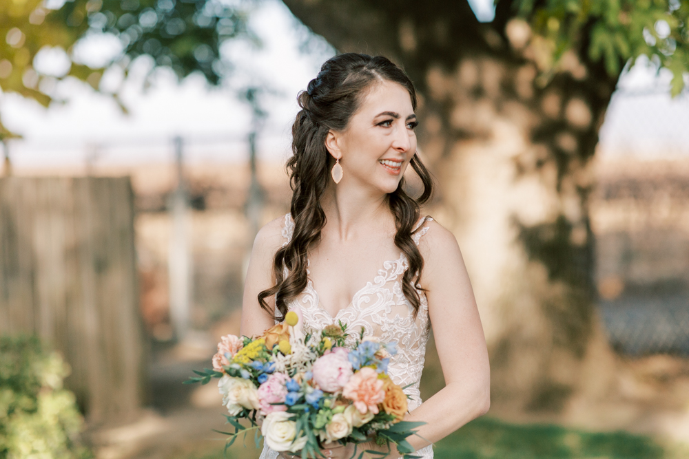 Bride with colorful bouquet and half up curled hair standing outside. 