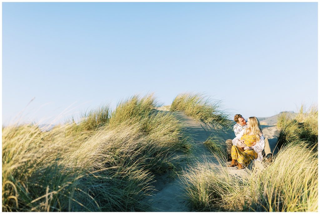 Couple sitting together talking in the tall grass in Morro Bay for beach maternity photos