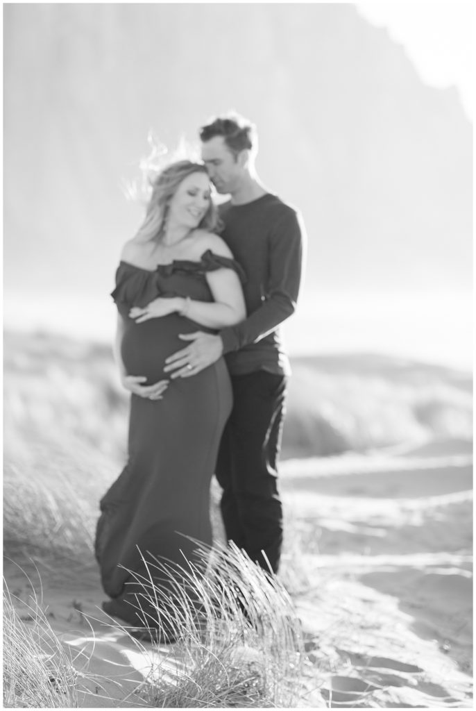 Man holding wife's baby bump from behind during beach maternity photos. 
